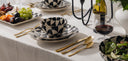 Dining table setting with black and white patterned dishes, gold cutlery, and fruit platter.