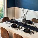 Dining table set with black plates, silverware, and wine glasses in a room with blue walls and wooden chairs.