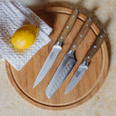 Set of knives on a wooden cutting board with a lemon and cloth napkin.