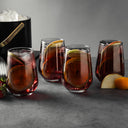A set of four angled stemless wine glasses with a smoke finish, displayed alongside a ice bucket with a gold handle and fruits around, suggesting a sophisticated drink setting.