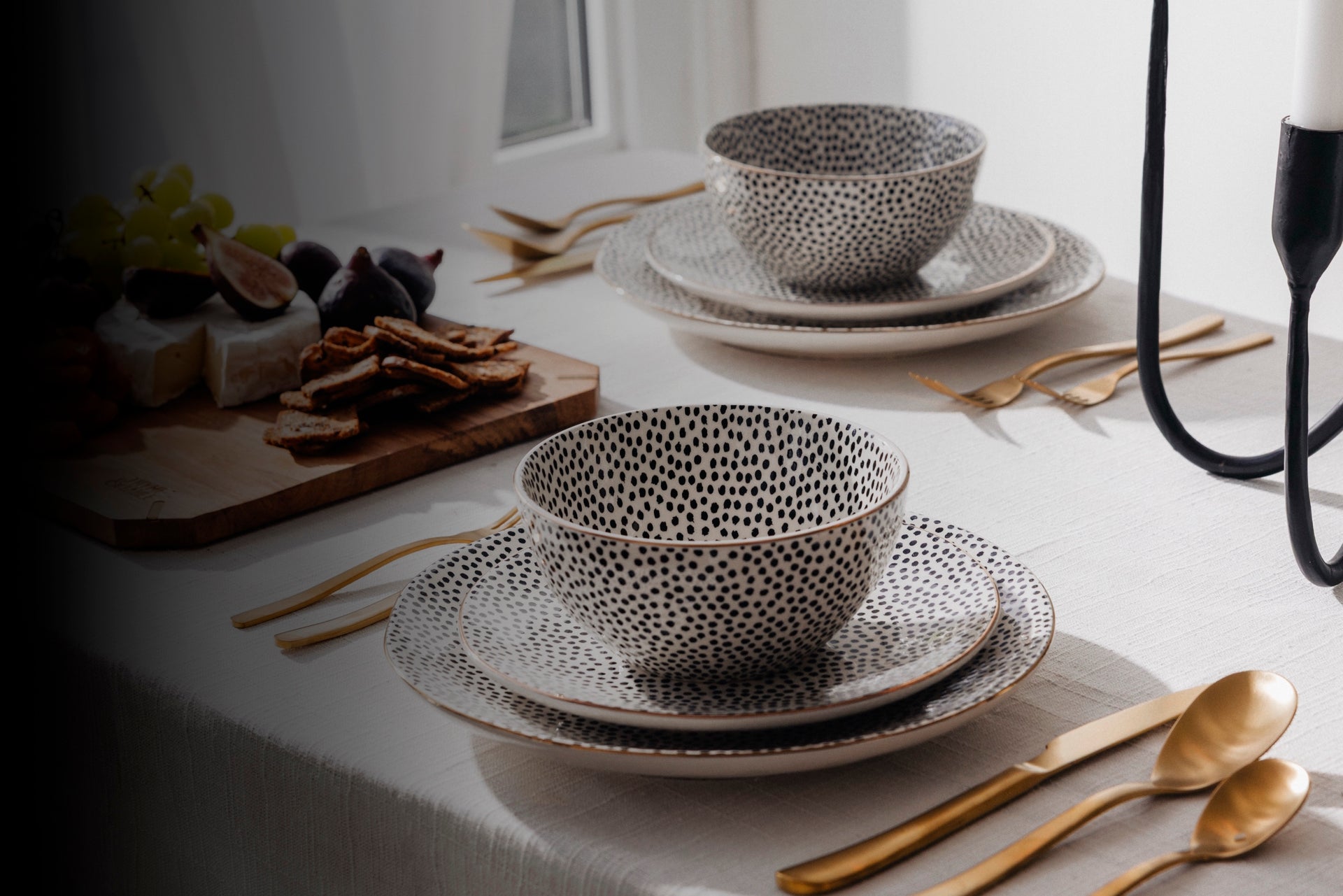 Dotted ceramic bowls and plates on a table with gold cutlery and a candle.