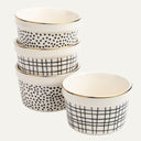 A set of four ceramic ramekins with black and white geometric patterns and gold trim.